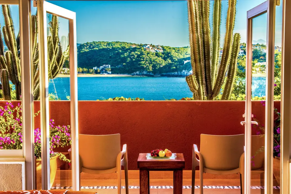 Junior Suite balcony with two chairs, cactus, flowers, and bay view at Las Brisas Huatulco.