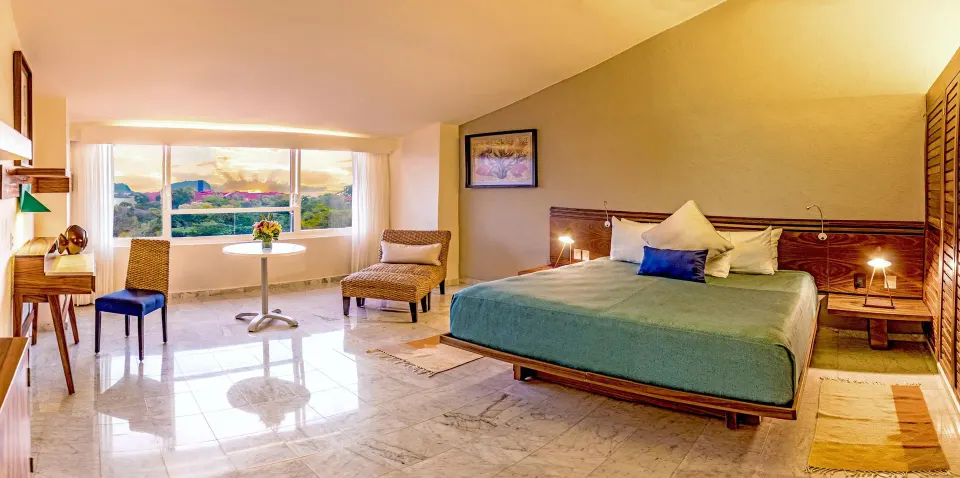 Junior Suite bedroom with a king bed, desk, seating, and wide window at Las Brisas Huatulco.