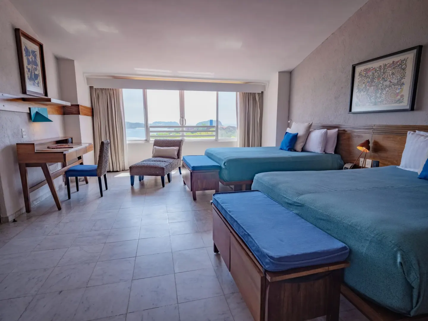 Junior Suite bedroom with two beds, desk, lounge chair, and water view at Las Brisas Huatulco.