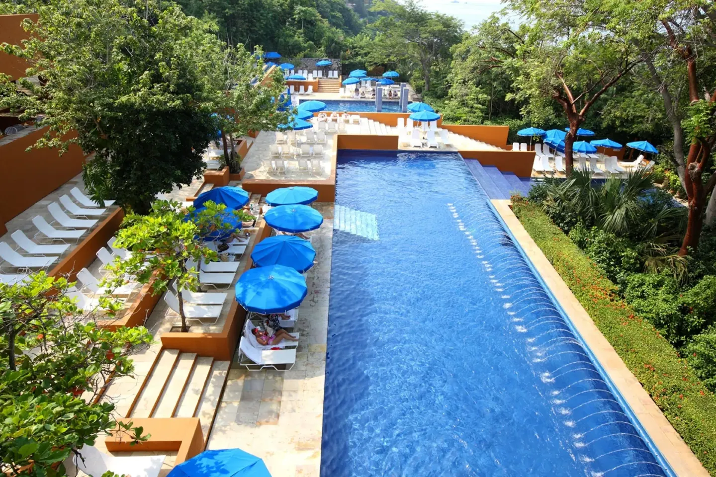 Long outdoor pool with blue umbrellas and lounge chairs at Las Brisas Ixtapa.