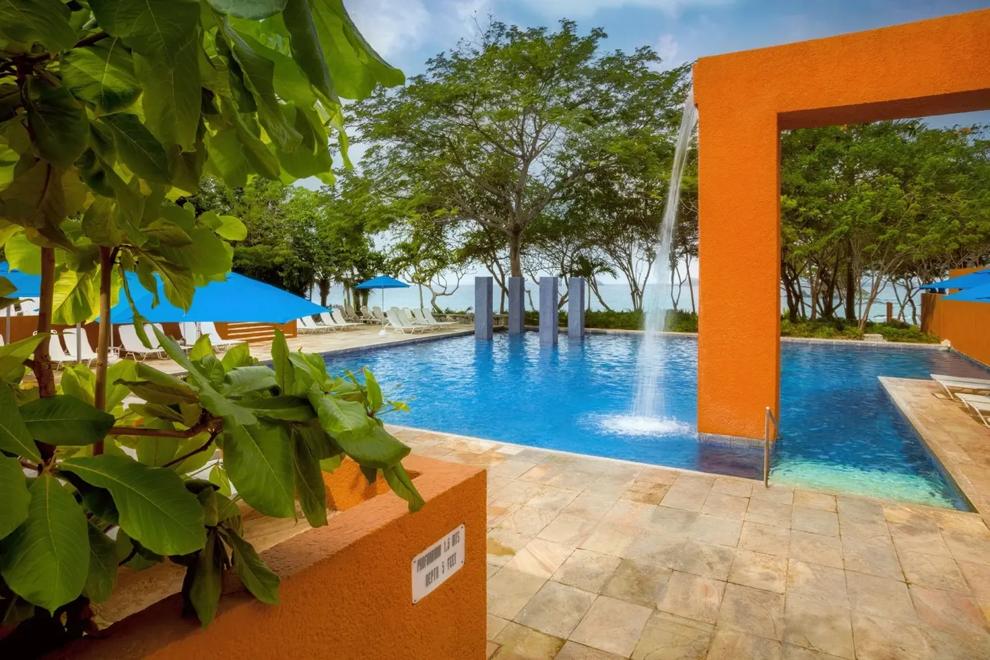Pool with fountain, blue umbrellas, trees, and orange arch at Las Brisas Ixtapa.