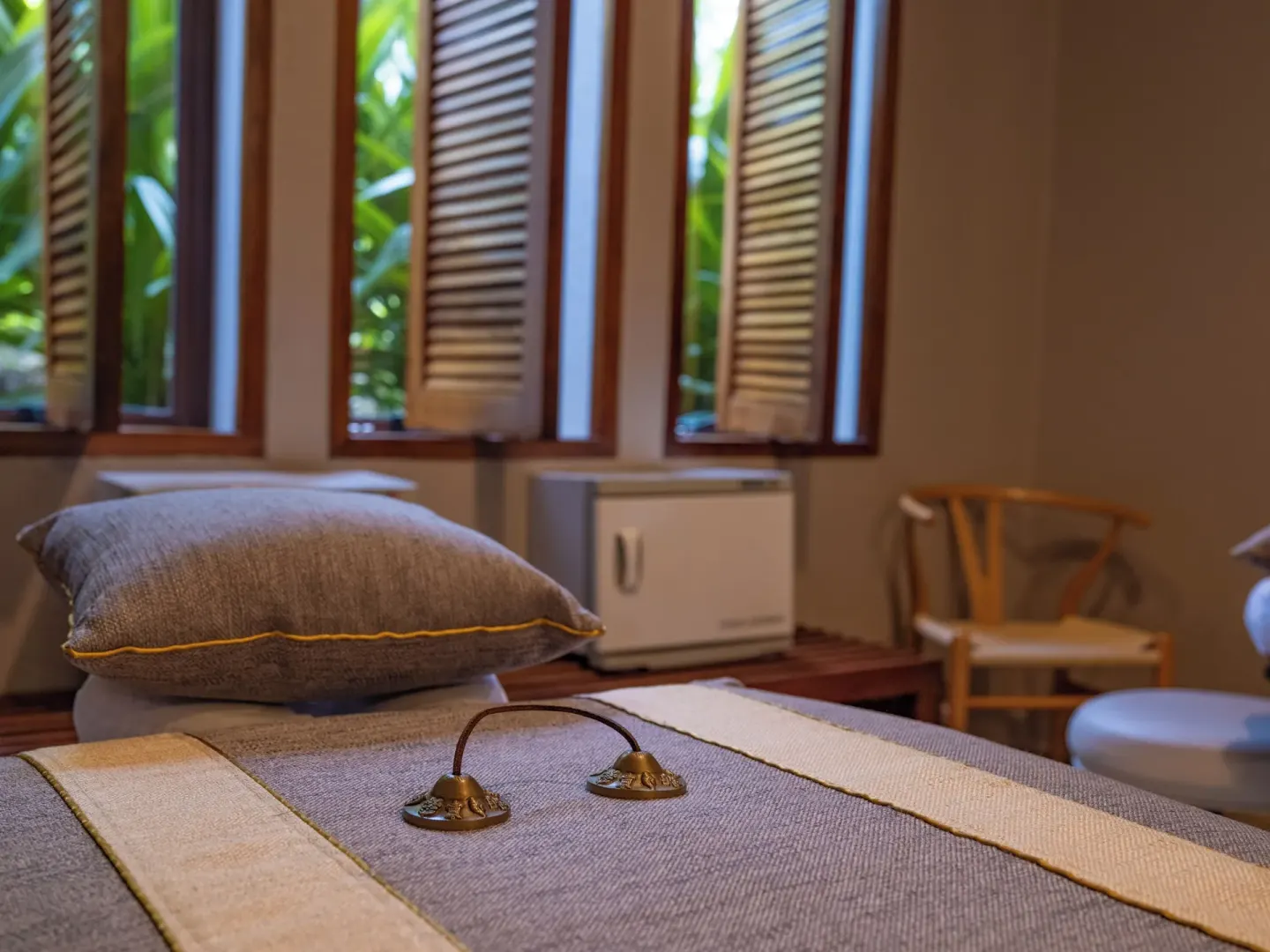 Spa treatment bed with cushion and brass bells by shuttered windows at Las Brisas Ixtapa.