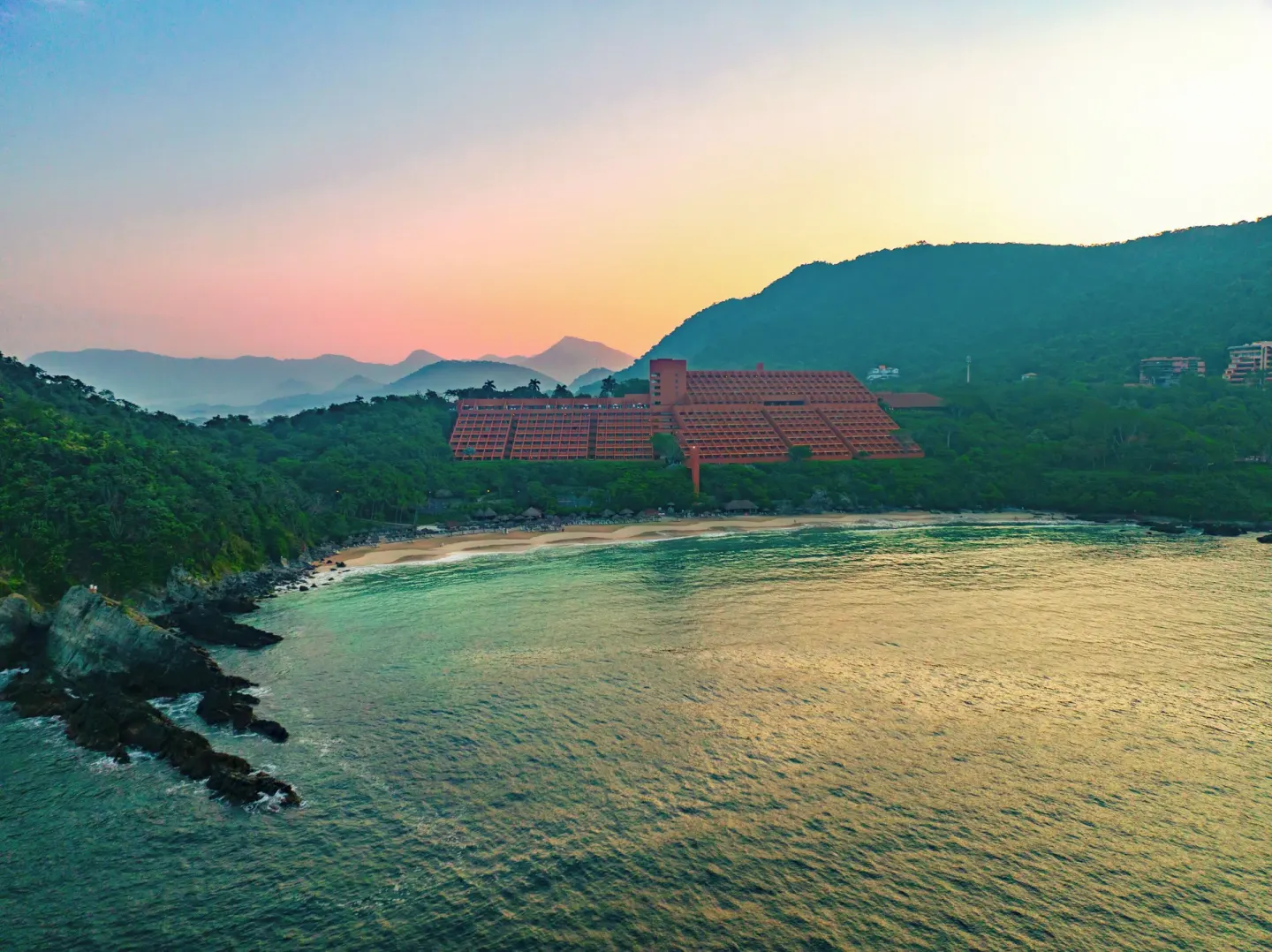 Las Brisas Ixtapa is seen across the bay at sunset with mountains behind it.