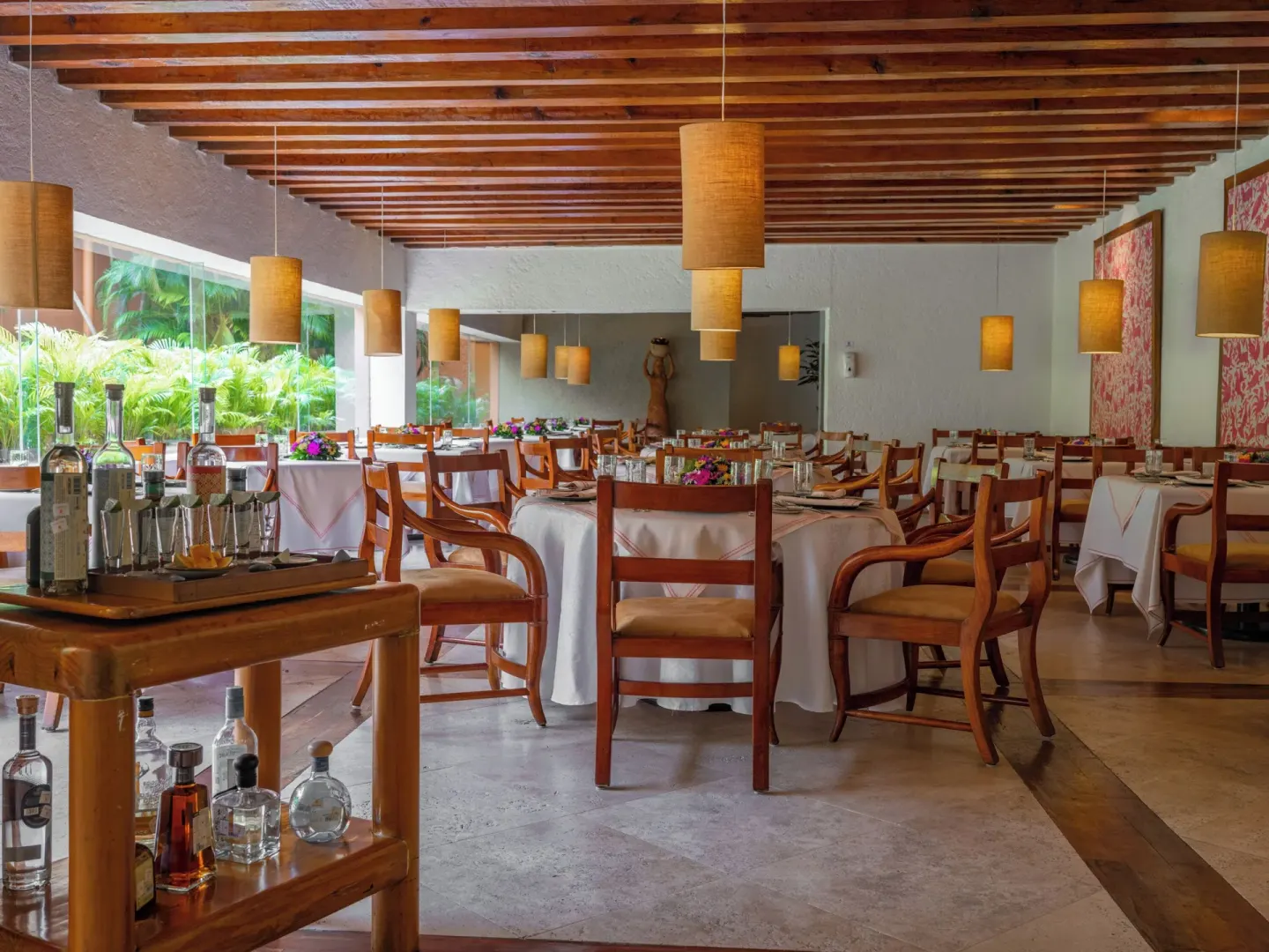 Restaurant dining room with wooden chairs, pendant lights, and bar cart at Las Brisas Ixtapa.