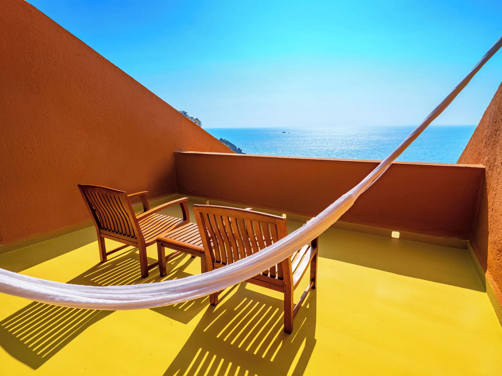 Deluxe Grand Bed balcony at Las Brisas Ixtapa with hammock, wooden chairs, and ocean view.