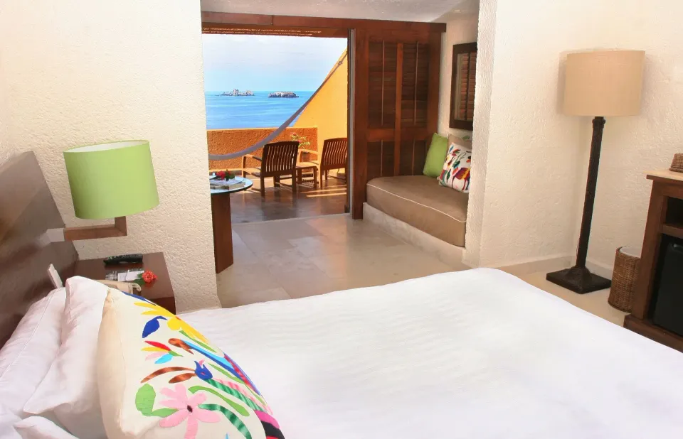 Deluxe Grand Bed guest room at Las Brisas Ixtapa with bed, sitting nook, balcony, and ocean beyond.