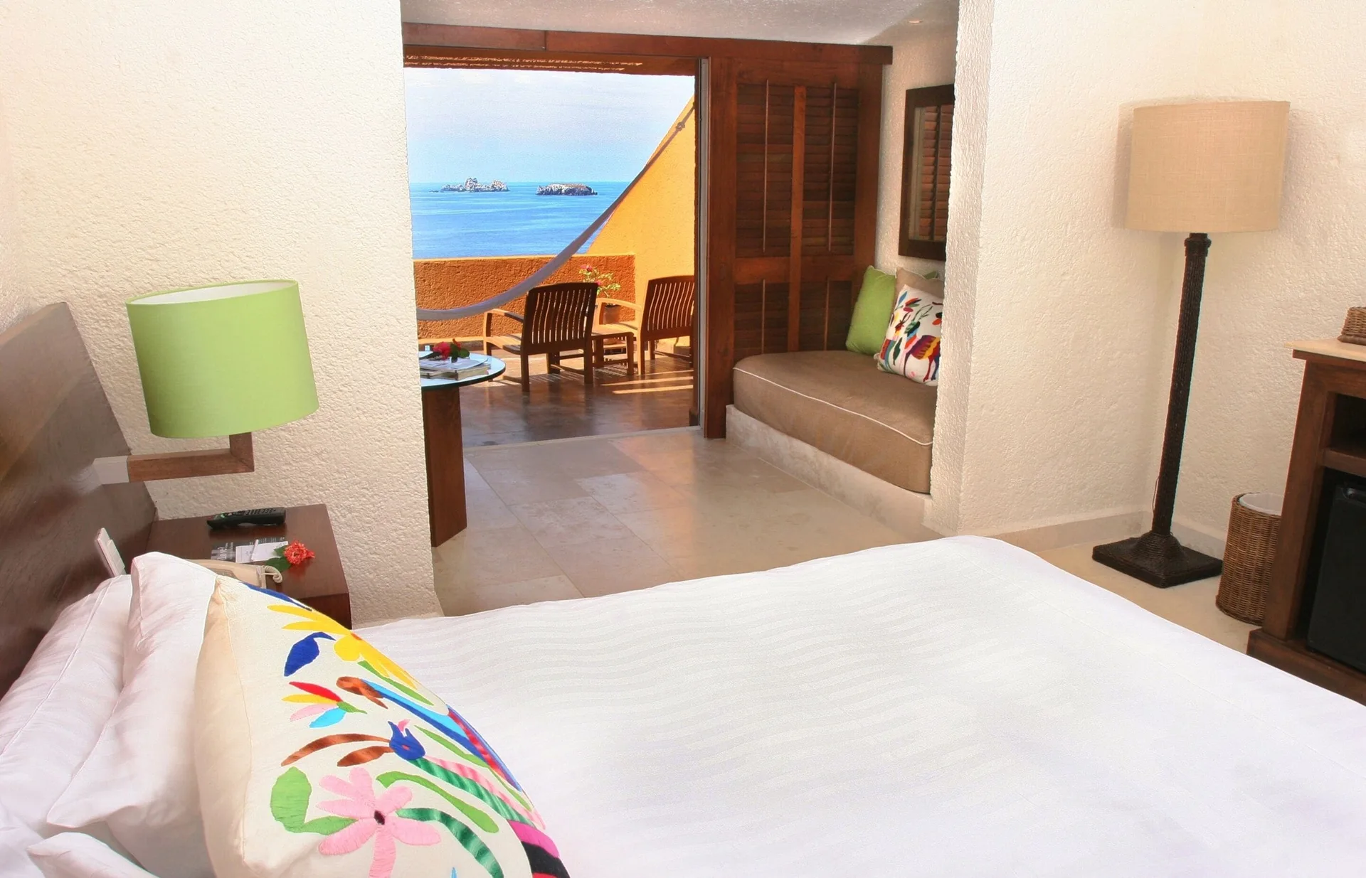 Deluxe Grand Bed guest room at Las Brisas Ixtapa with bed, sitting nook, balcony, and ocean beyond.