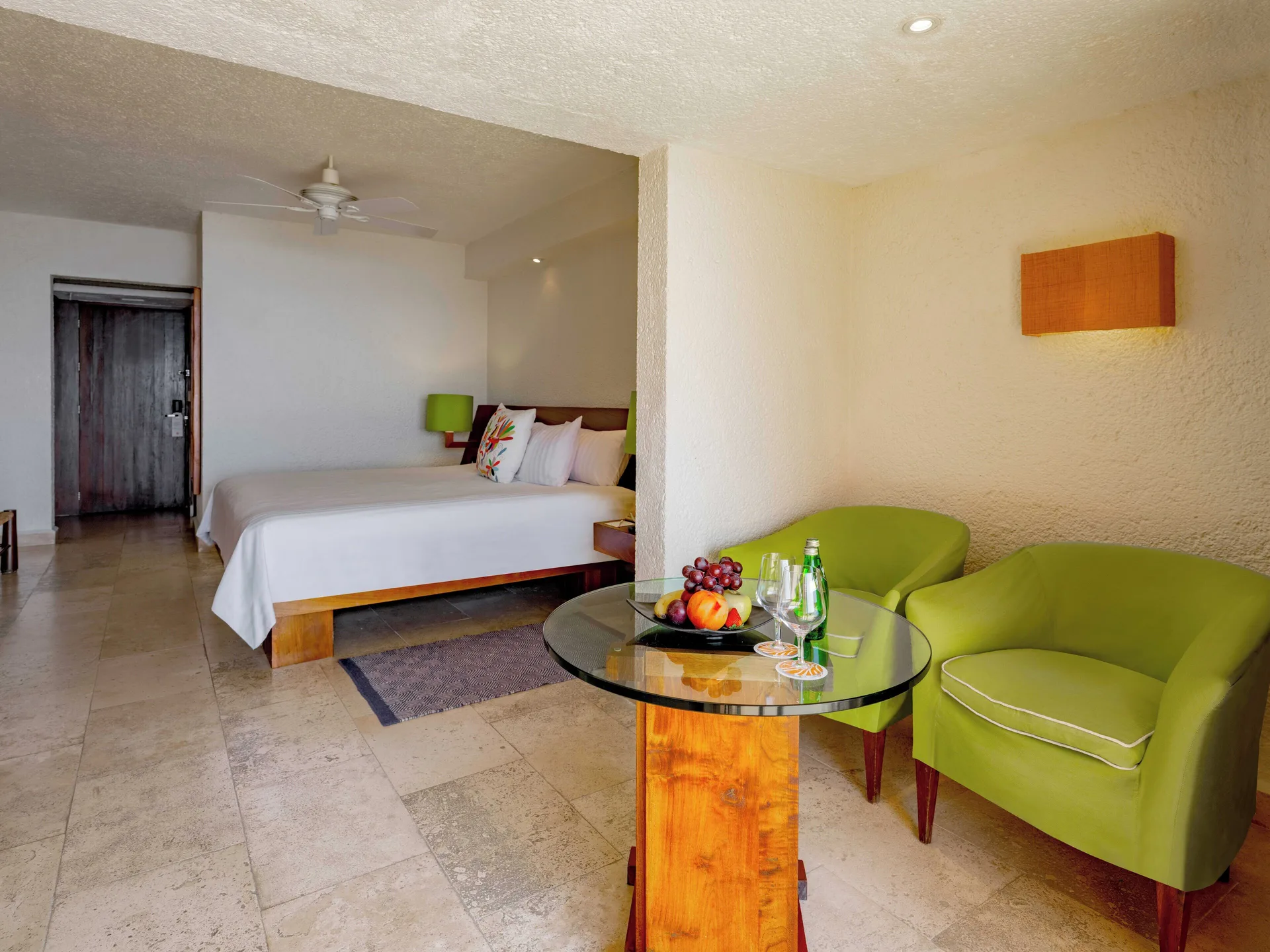 Deluxe Grand Bed room at Las Brisas Ixtapa with bed, green chairs, glass table, and fruit plate.