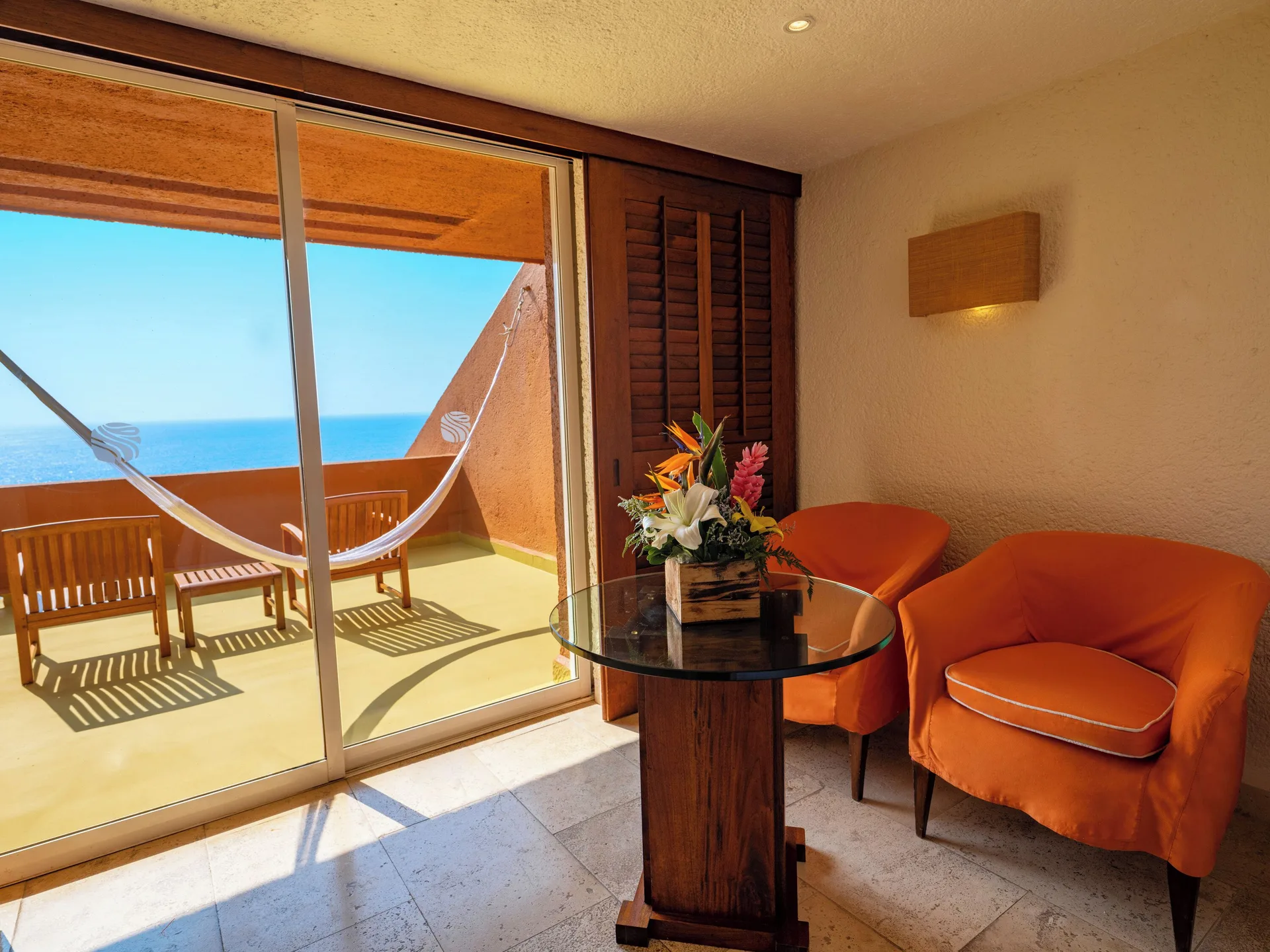 Deluxe Grand Bed sitting corner at Las Brisas Ixtapa with orange chairs, table, balcony, and hammock.