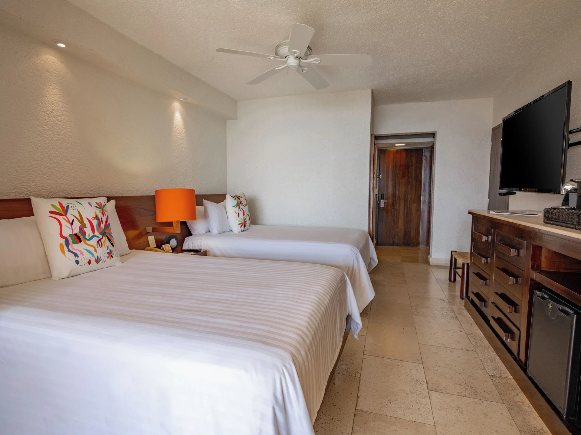 Deluxe Grand room with two beds, ceiling fan, TV, and minibar at Las Brisas Ixtapa.