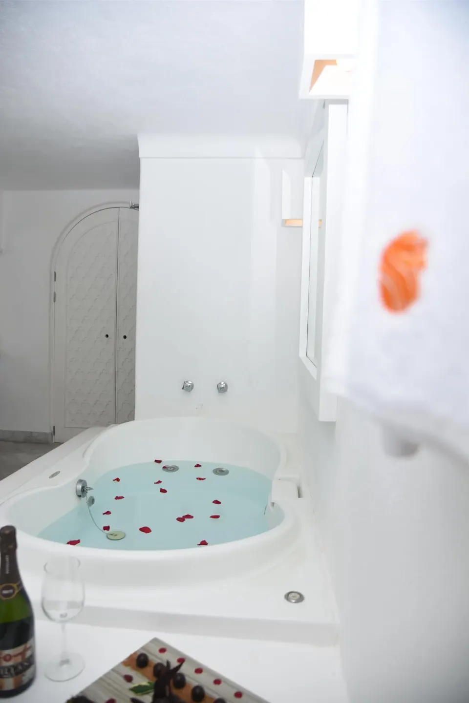 White bathroom with filled jetted tub, rose petals, and bottle setup at Las Hadas.
