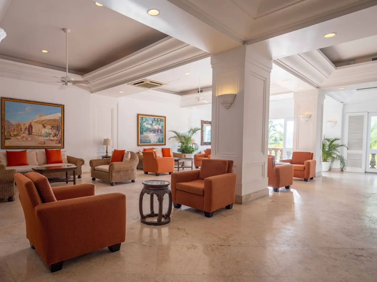 Bright lobby seating area at Las Hadas with orange chairs, wicker sofas, and framed art.