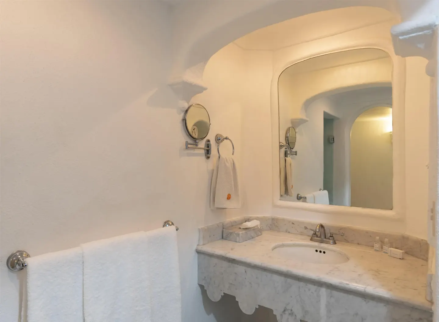 White bathroom vanity with marble counter and arched mirror at Las Hadas.