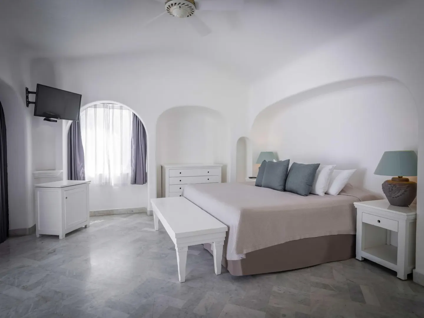King bed guest room with arched window and wall-mounted TV at Las Hadas.