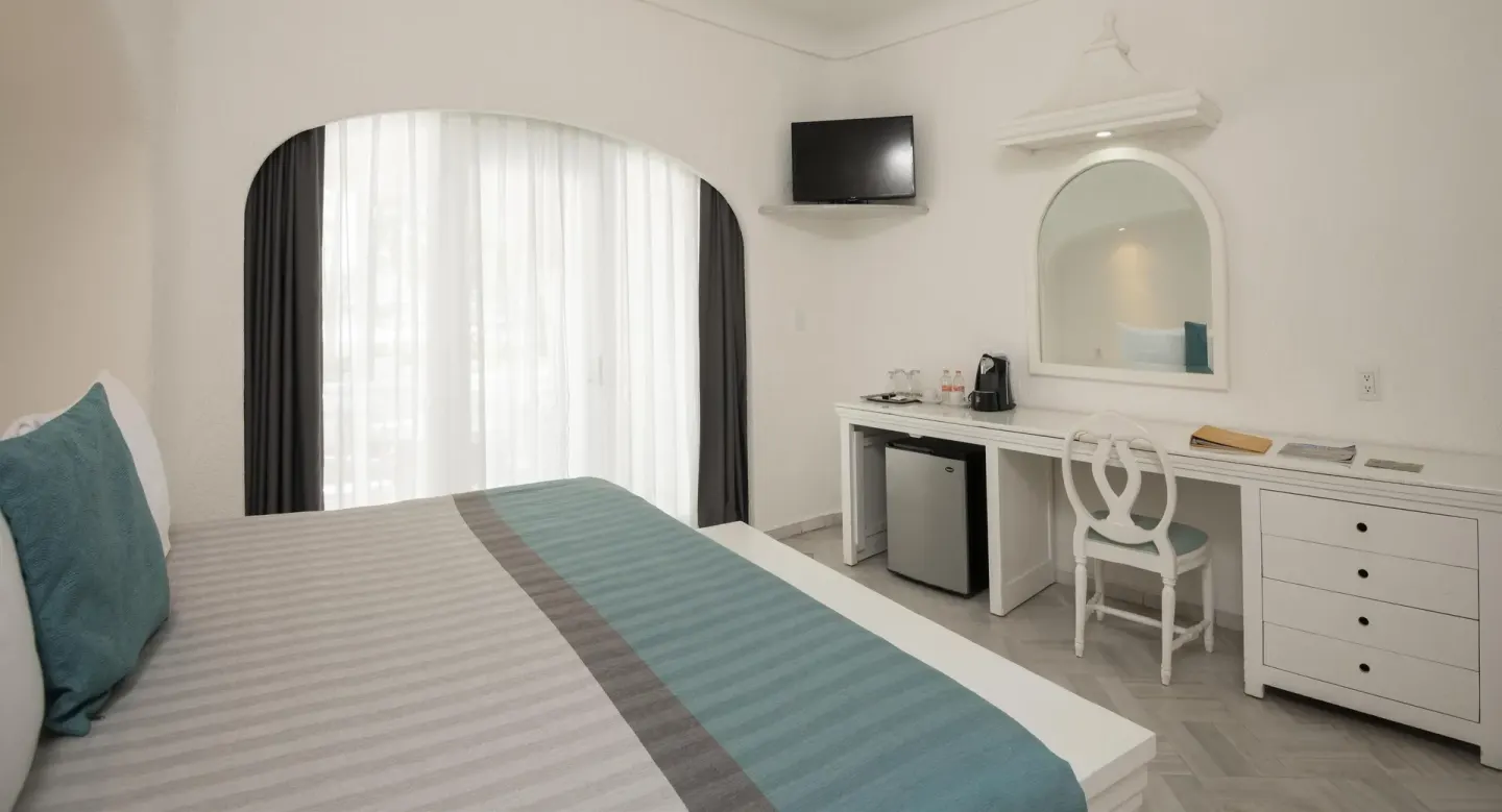 King bed guest room with desk, mini fridge, and arched window at Las Hadas.