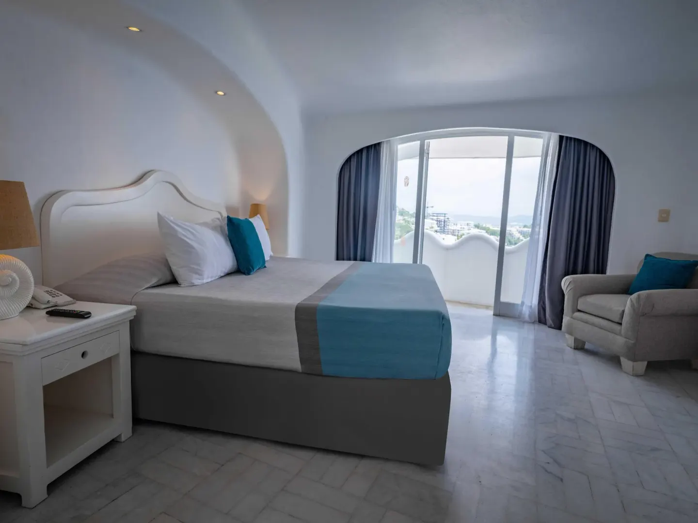Guest room with king bed, armchair, balcony doors, and distant view at Las Hadas.