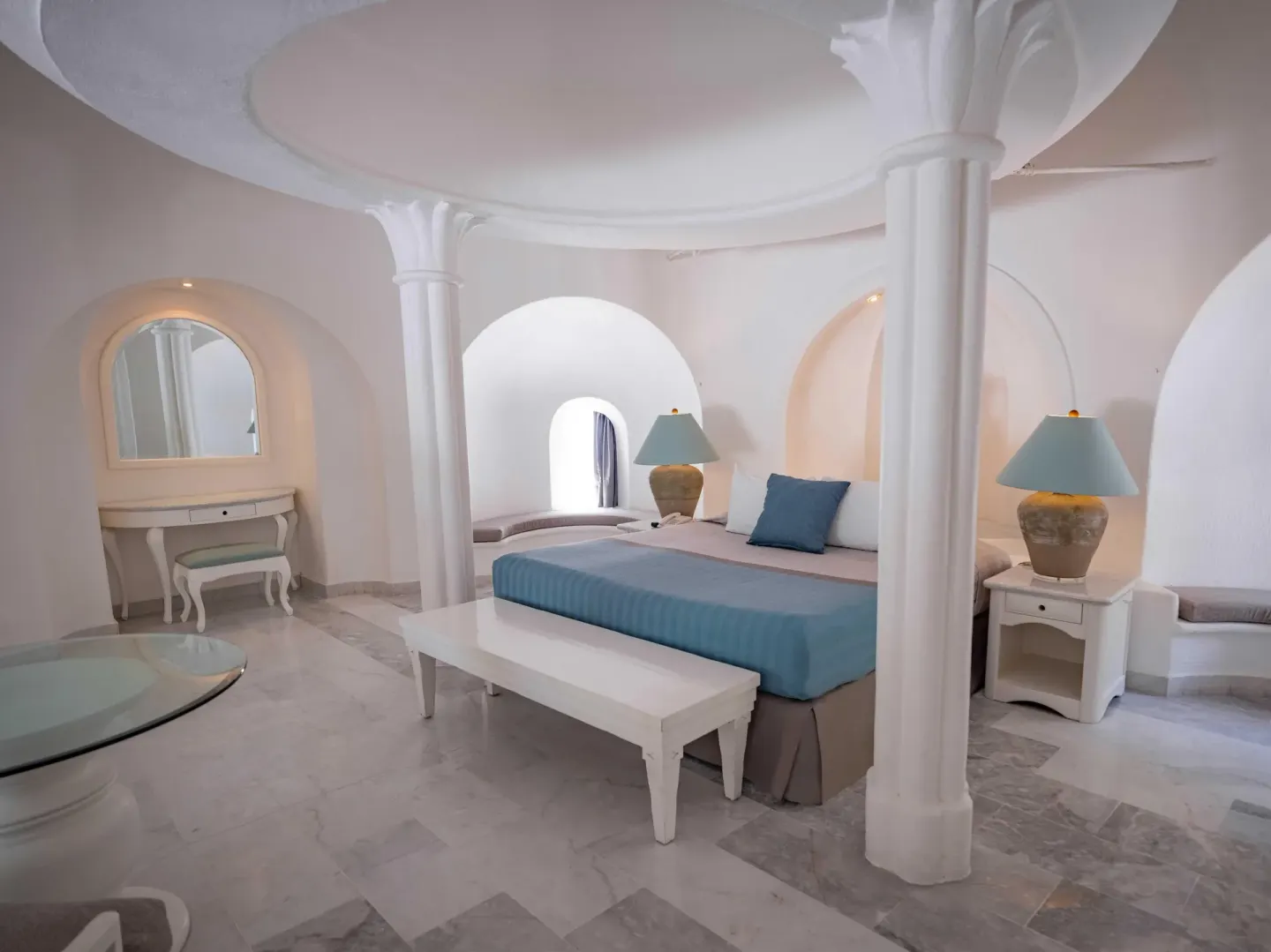 Guest room with king bed, canopy-like columns, vanity, and arched alcoves at Las Hadas.