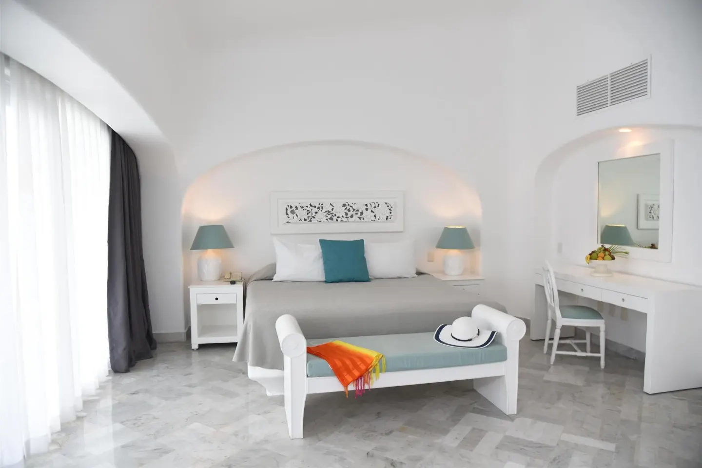 Guest room with king bed, bench, vanity, and arched white walls at Las Hadas.