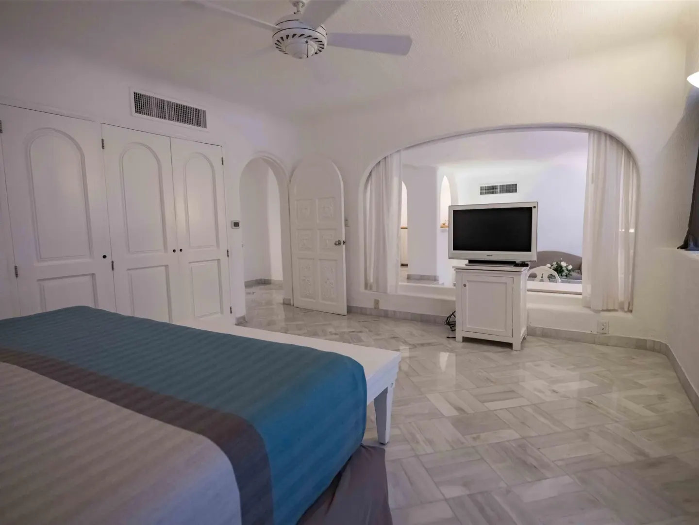 King bed guest room with TV cabinet and large interior arch at Las Hadas.
