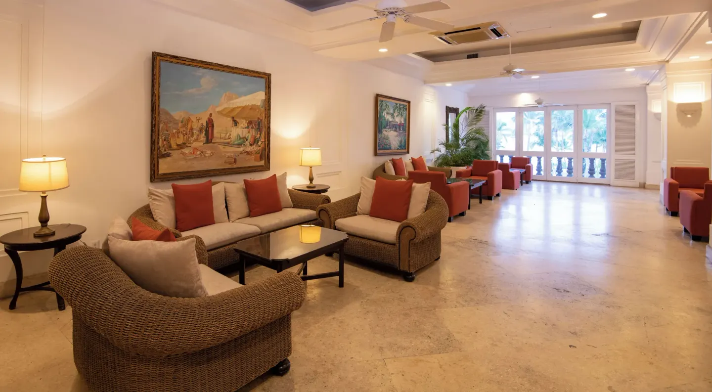 Lobby seating corridor at Las Hadas with wicker chairs, red cushions, artwork, and balcony doors.