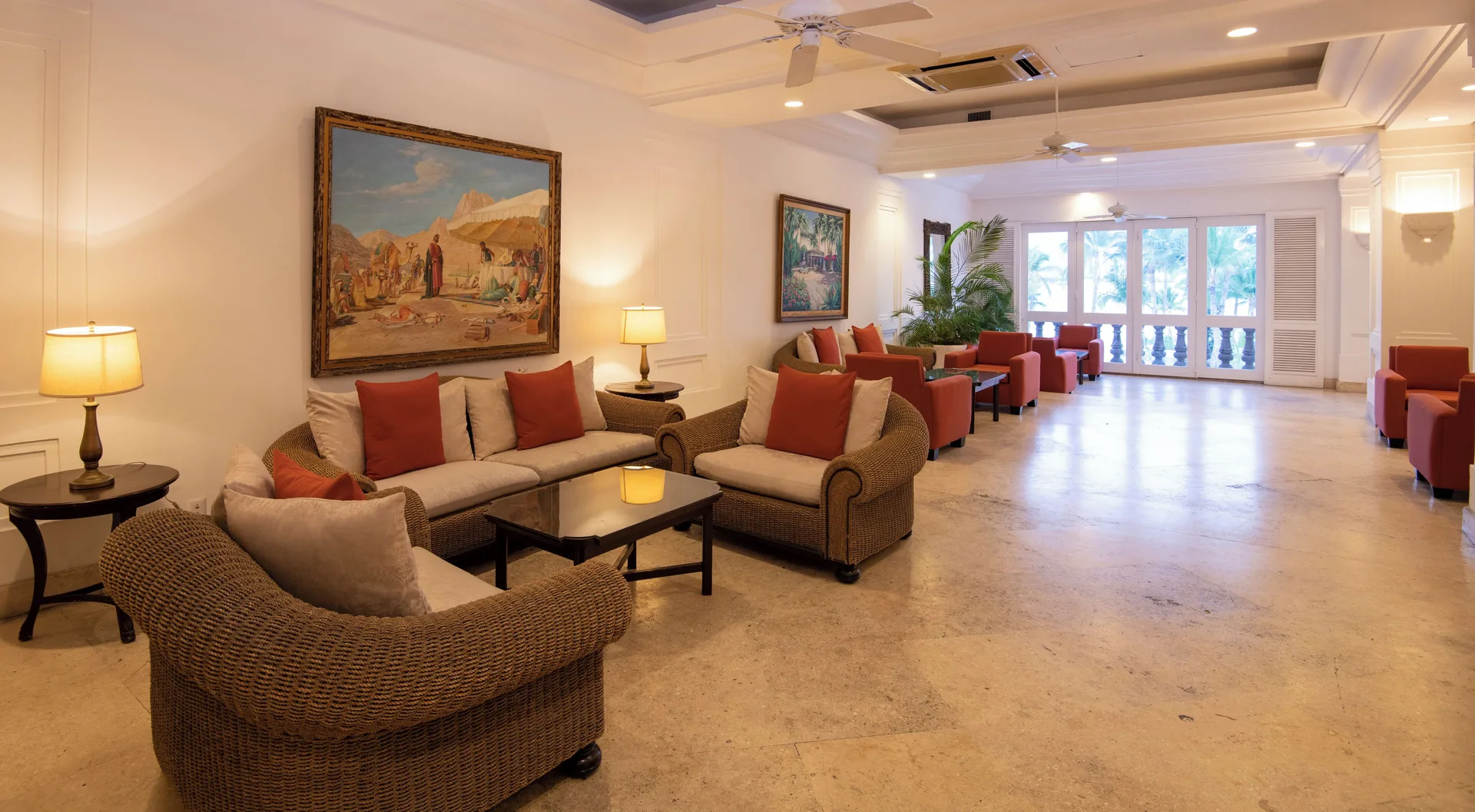 Lobby seating corridor at Las Hadas with wicker chairs, red cushions, artwork, and balcony doors.