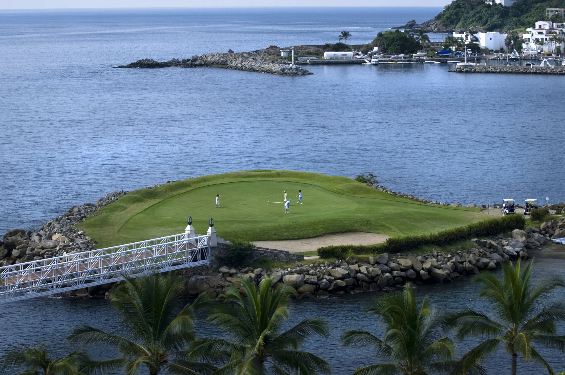 Golf green on a rocky point with ocean water and a white bridge at Las Hadas.