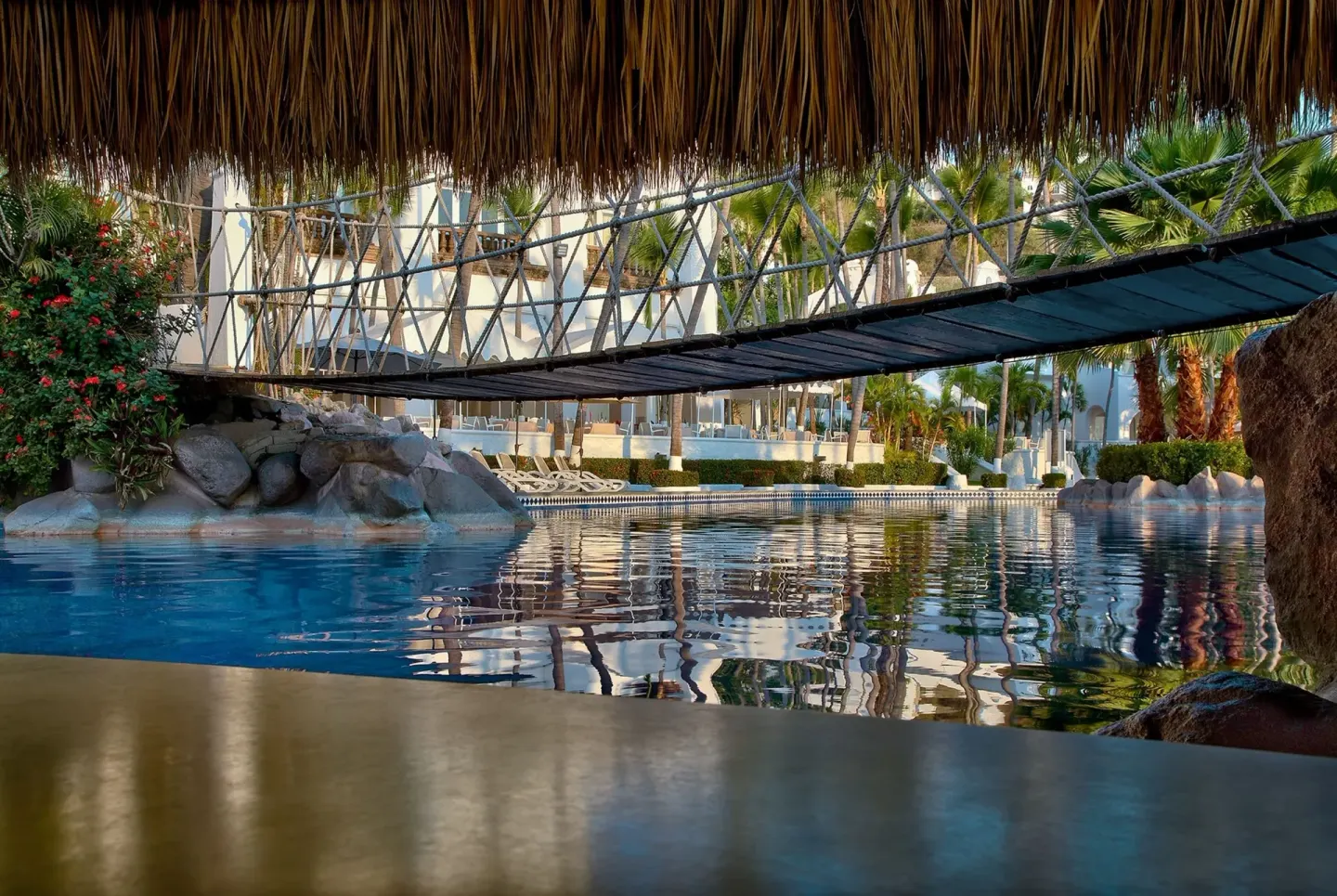 A footbridge crosses the resort pool beneath a thatched roof at Las Hadas.