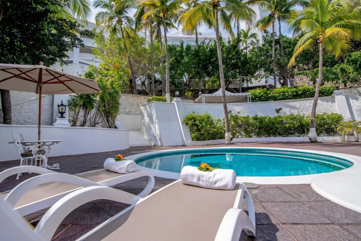 Secluded pool patio with loungers, umbrella, and palm landscaping at Las Hadas.