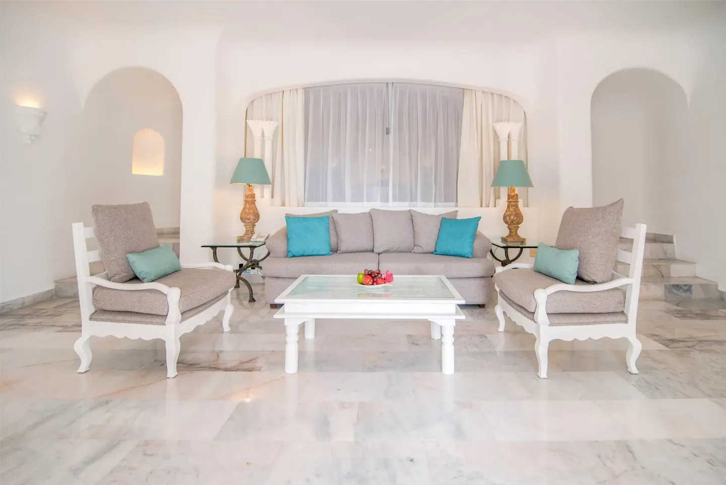 Suite sitting area with sofa, armchairs, glass coffee table, and arched niches at Las Hadas.