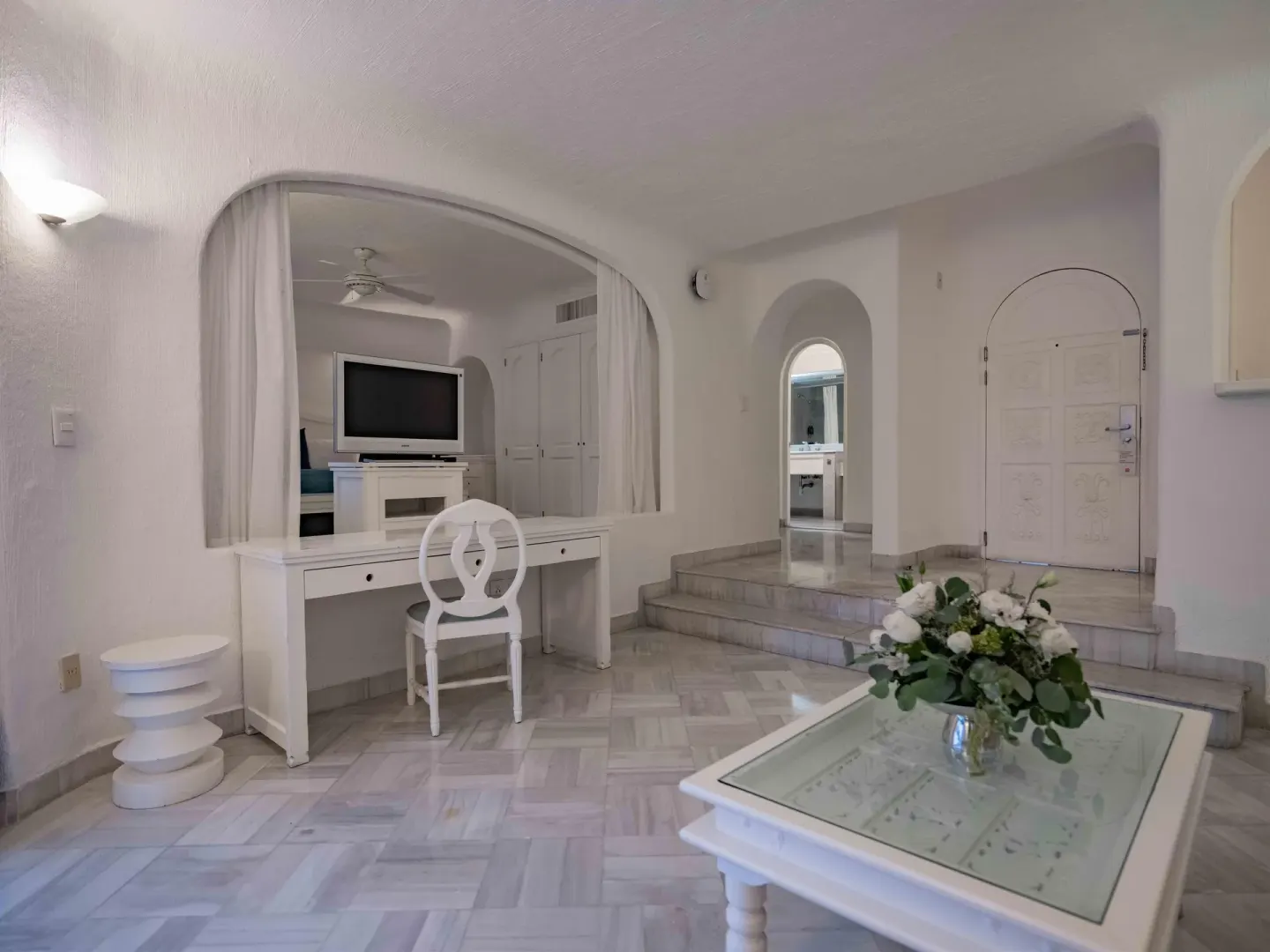 White suite living area with vanity, TV, coffee table, and arched entry at Las Hadas.