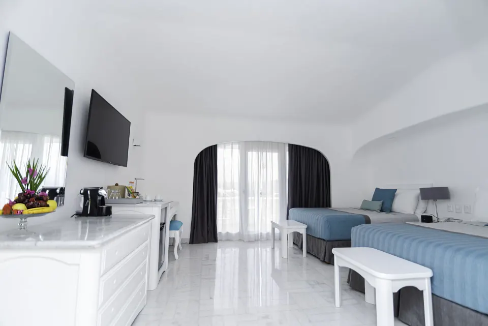 Brisas Beach Club room with two beds, dresser, TV, and balcony curtains at Las Hadas.