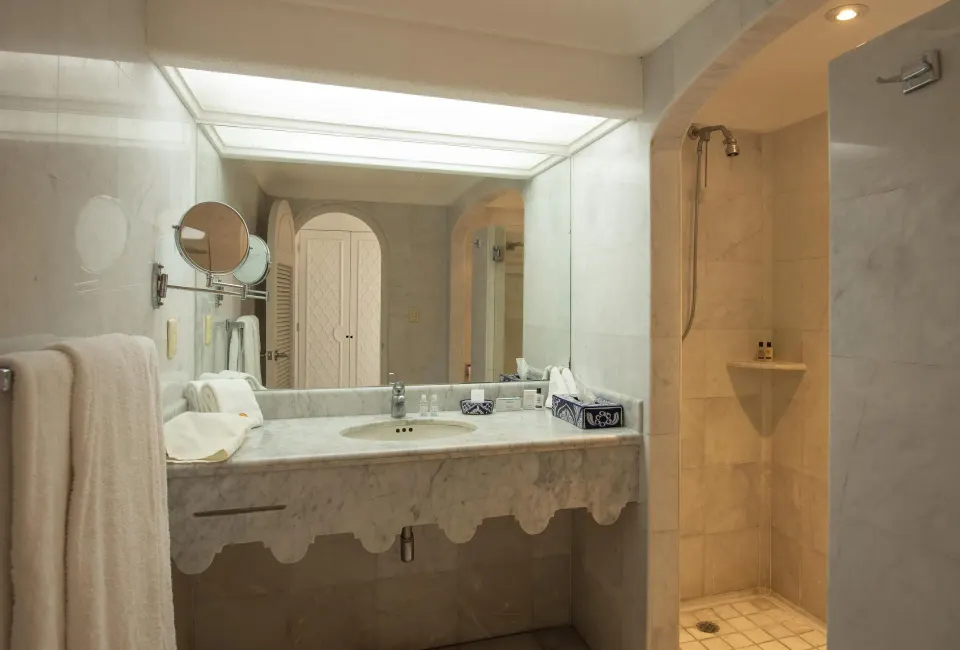 Deluxe Room bathroom with marble vanity, large mirror and walk-in shower at Las Hadas.