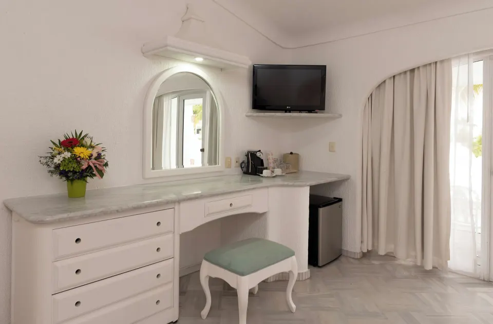 Deluxe Room vanity wall with TV, dresser, stool and balcony curtains at Las Hadas.