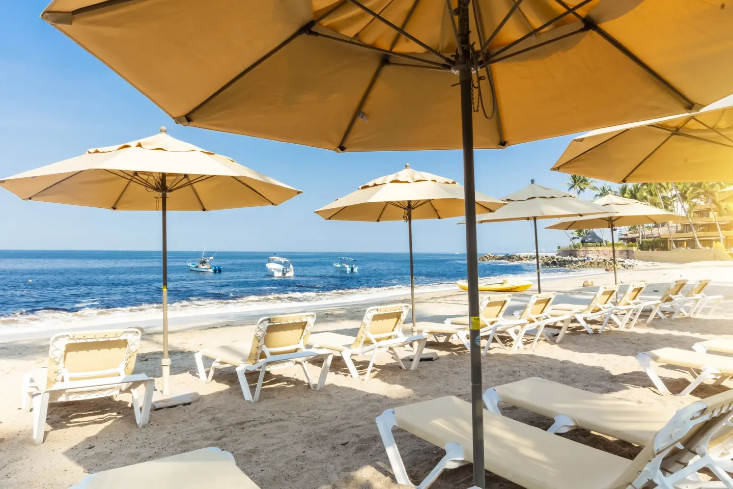 Beach loungers and umbrellas at Las Palmas by the Sea face the ocean with small boats offshore.