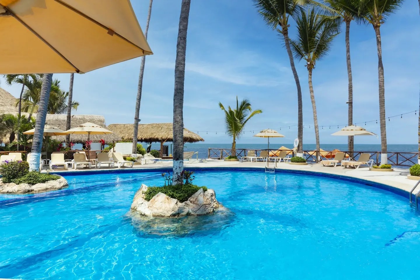 Curved oceanfront pool at Las Palmas by the Sea with palms, loungers, and umbrellas.