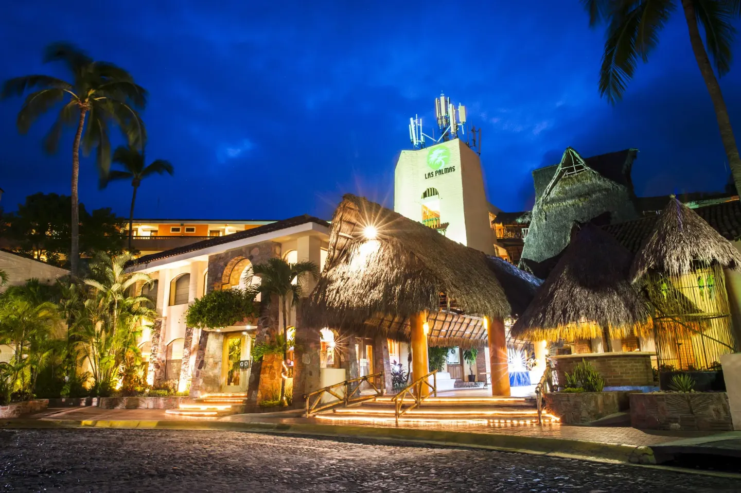 Night view of the illuminated entrance and palapa roofs at Las Palmas by the Sea.