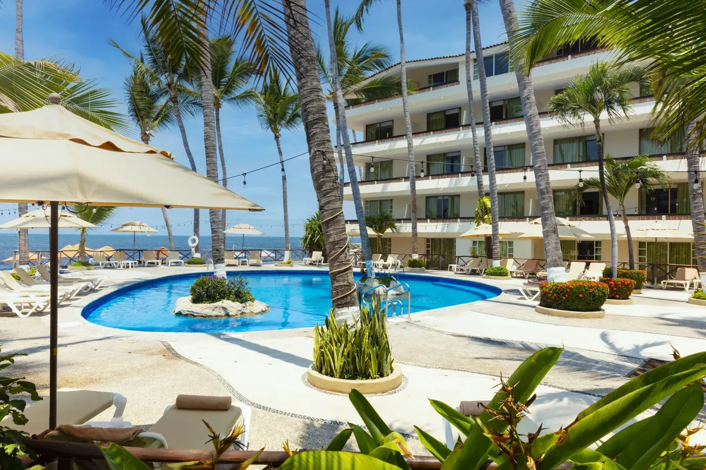 Curved pool, loungers, palms and oceanfront building at Las Palmas by the Sea.