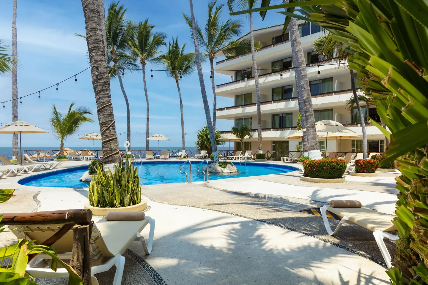 Palm-lined pool courtyard at Las Palmas by the Sea with loungers, umbrellas, and ocean beyond.