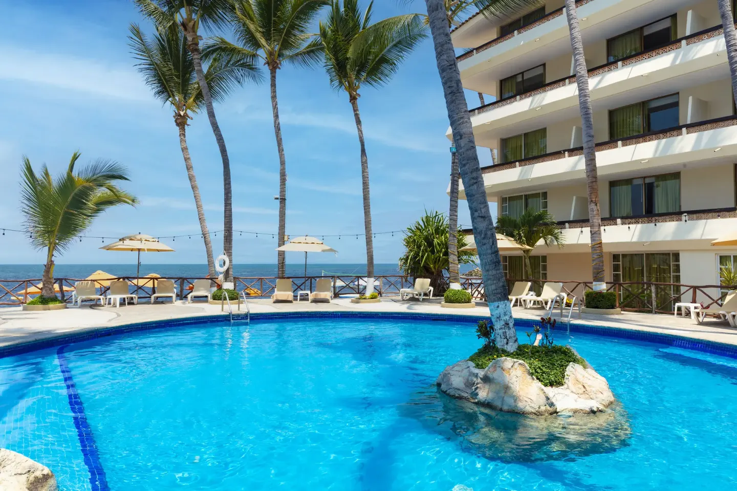 Pool with palm island, loungers, umbrellas and ocean view at Las Palmas by the Sea.