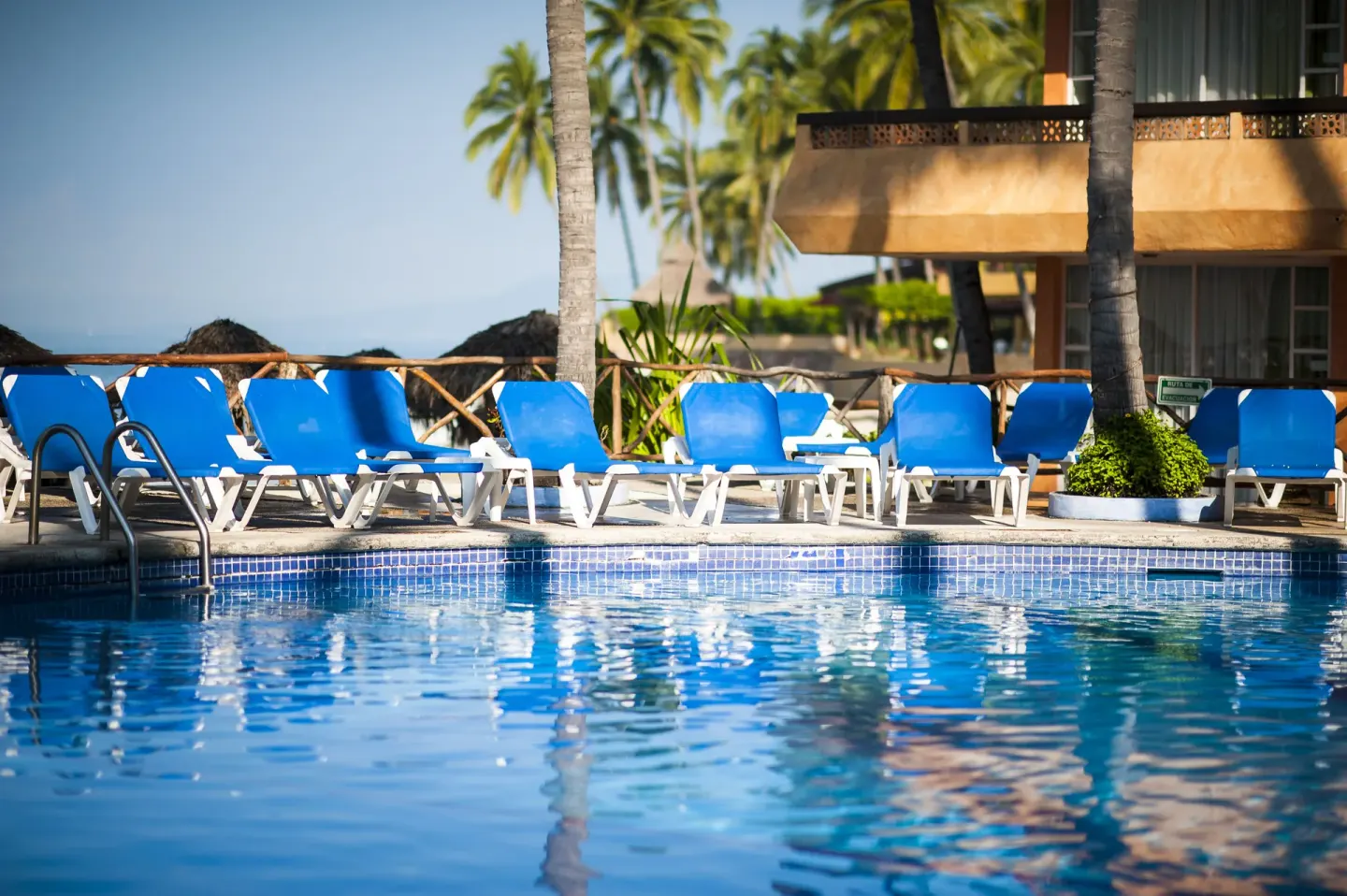 Poolside blue loungers at Las Palmas by the Sea with water reflections and palms behind.