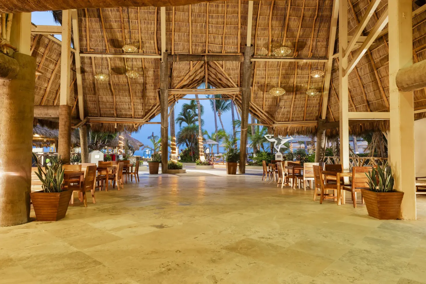 Open-air palapa seating area at Las Palmas by the Sea with wood tables and ocean beyond.