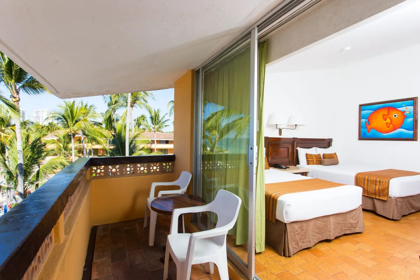 Ocean View Room balcony with chairs and two beds inside at Las Palmas by the Sea.