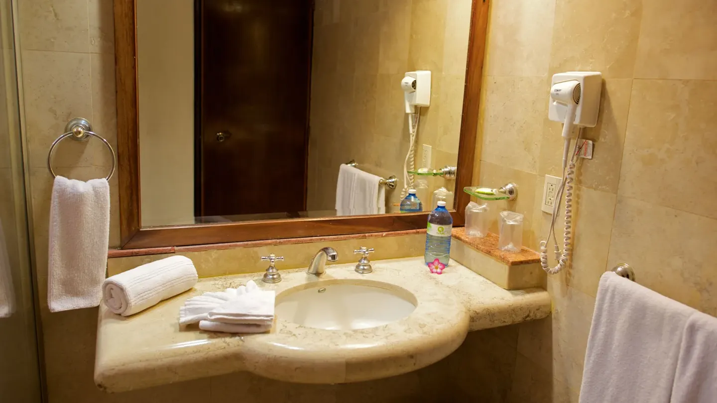 Standard Room bathroom vanity with sink, mirror, towels, hair dryer, and bottled water at Las Palmas by the Sea.