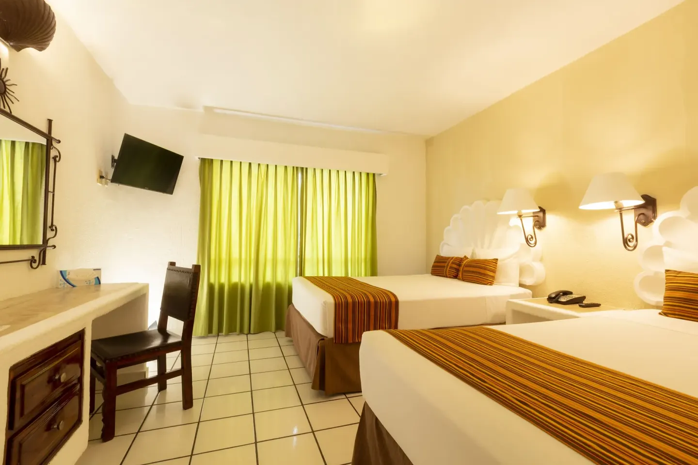 Standard Room with two beds, desk chair, wall mirror, TV, and green curtains at Las Palmas by the Sea.