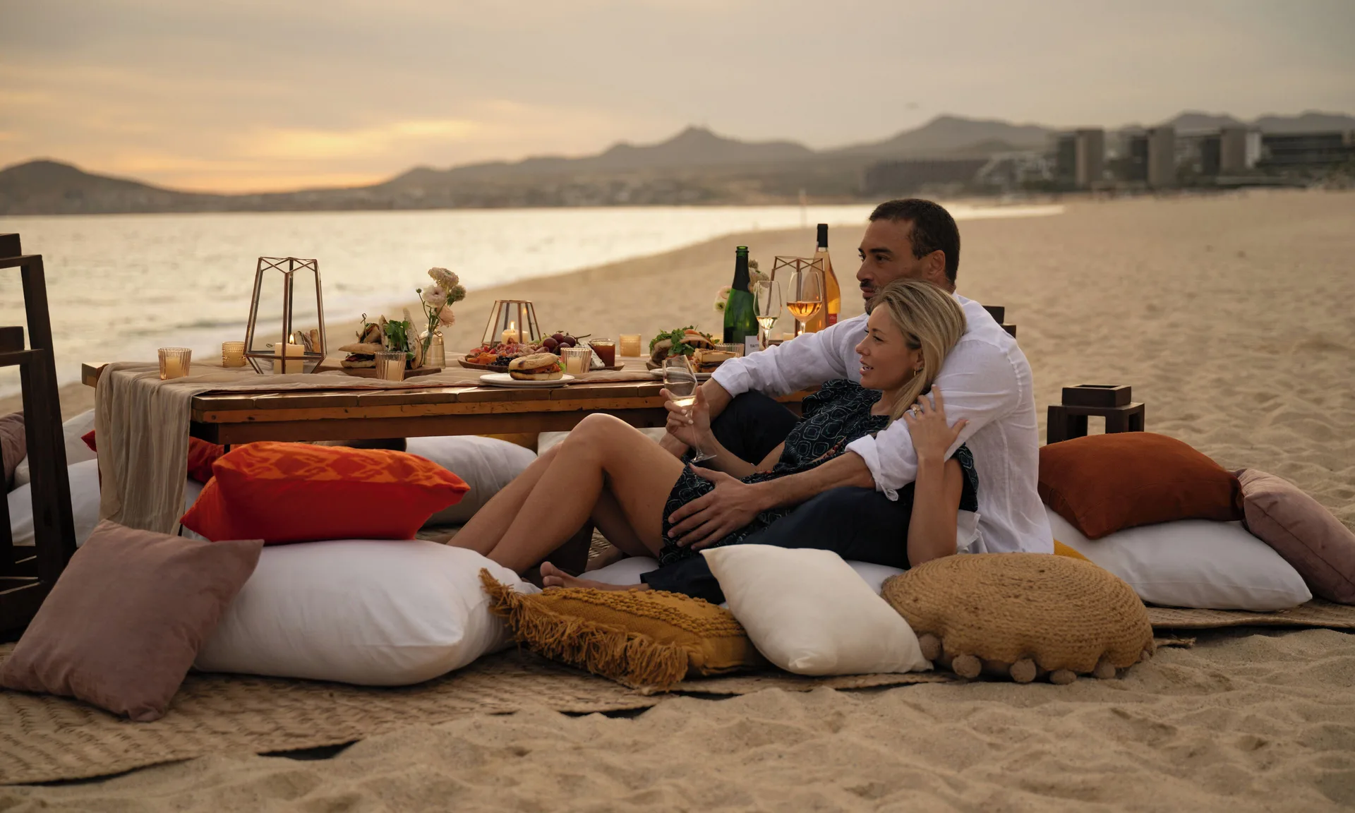 Couple relaxes on beach pillows beside a low dining table at Las Ventanas al Paraiso.