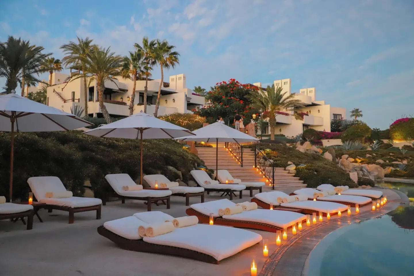 Poolside loungers with candles and resort buildings at Las Ventanas al Paraiso.