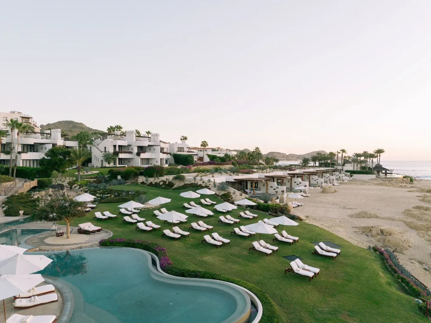 Resort grounds with pool, lawn loungers, white buildings, and beach at Las Ventanas al Paraiso.