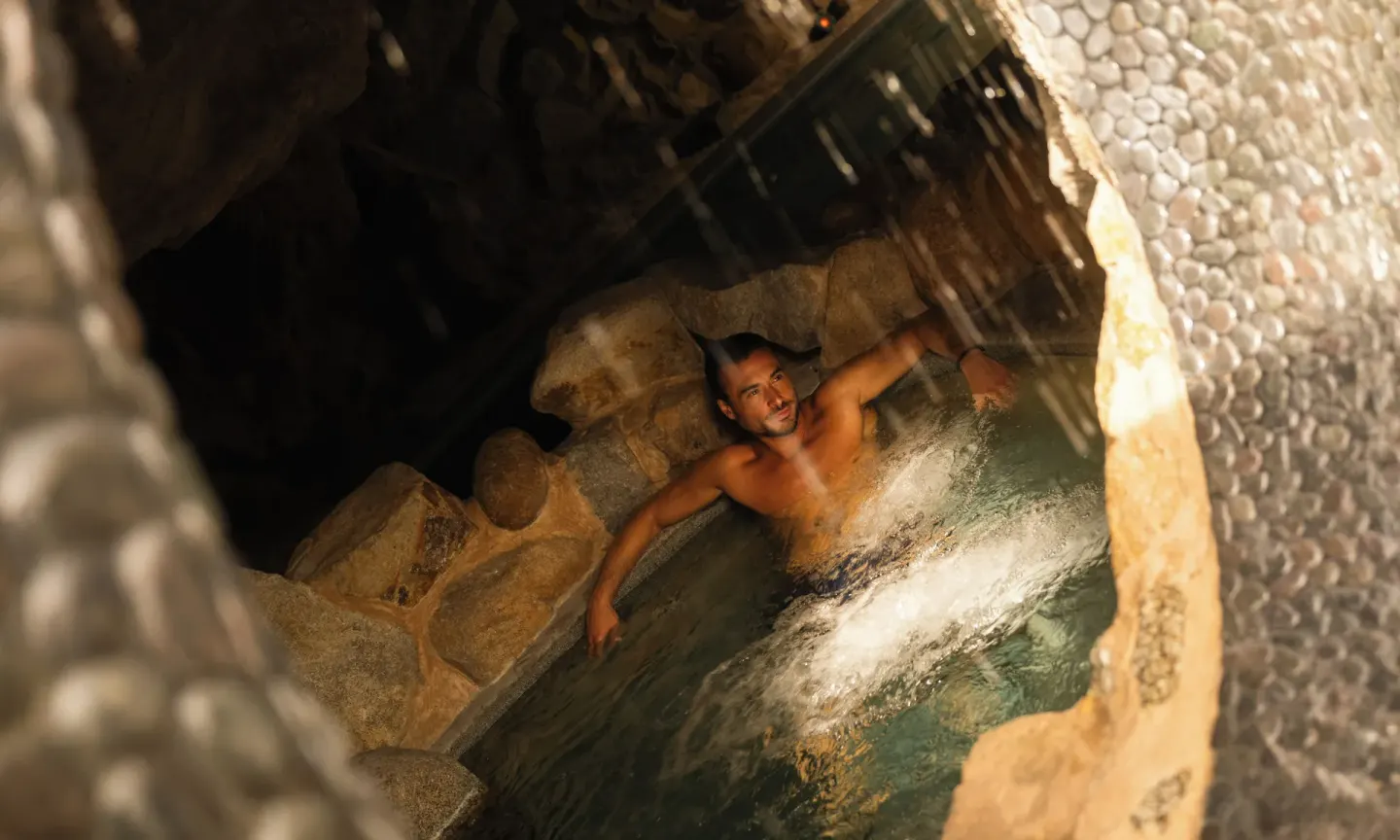 Guest sitting in a rock-lined spa pool under falling water at Las Ventanas al Paraiso.