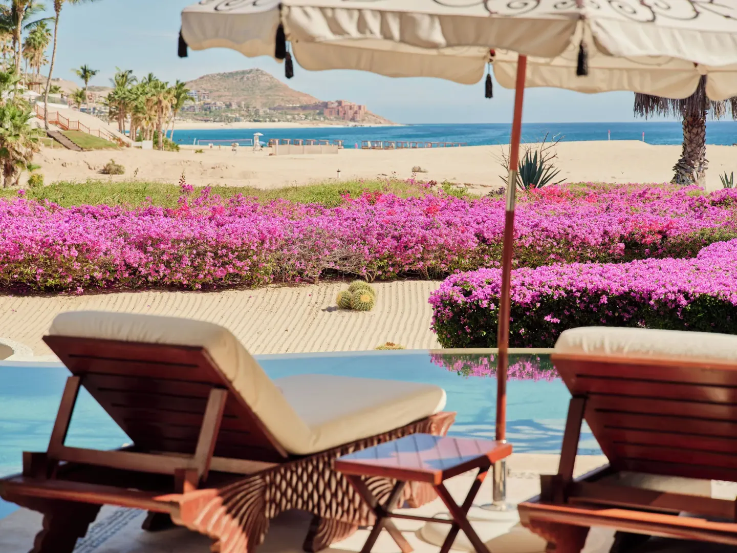 Villa pool loungers under an umbrella with beach and ocean beyond at Las Ventanas al Paraiso.