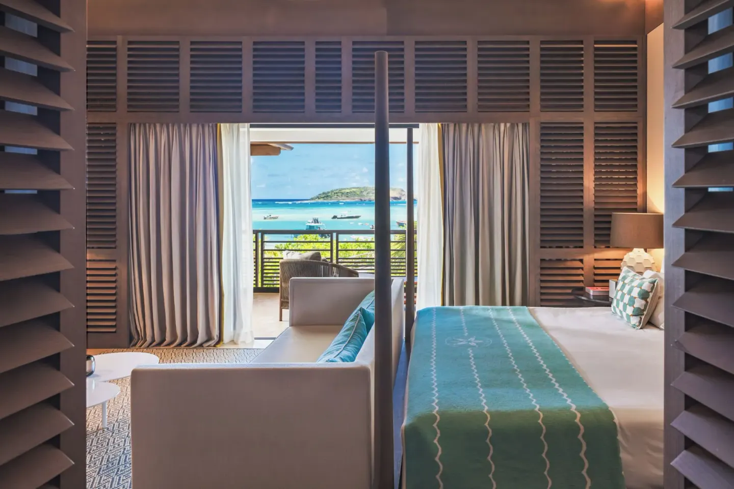 Guest room bed and sofa facing a turquoise bay at Le Barthélemy Hotel & Spa.